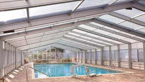 Una piscina coperta con pavimento in mattoni, pareti in vetro e struttura a tetto.