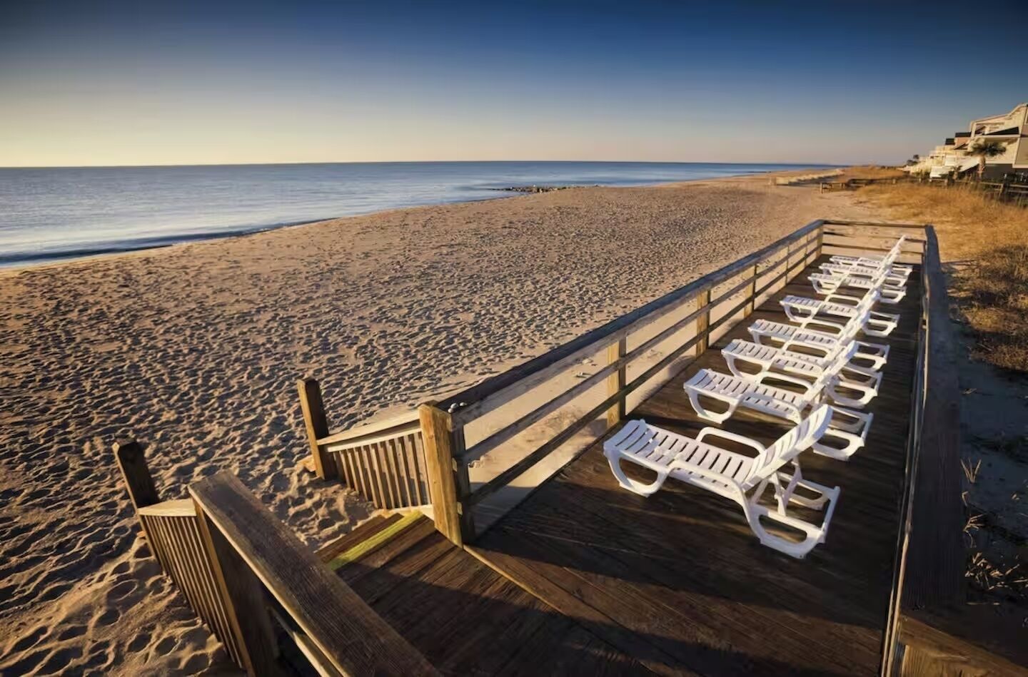 Ein Strand mit einer Holzterrasse und weißen Liegestühlen.
