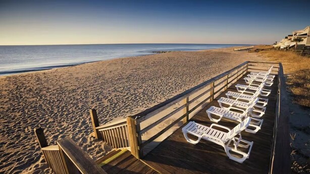 Una spiaggia con un pontile di legno e poltrona da spiaggia bianche.