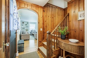 A wooden staircase leading to a living area with a sofa, a potted plant, and a framed picture on the wall. - Brighton Stay Near URMC | King Bed, Home Cinema & Backyard (Rochester)