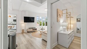 Ein modernes Wohnzimmer mit Flachbildfernseher, einer Couch, einem Couchtisch und einer Lampe.