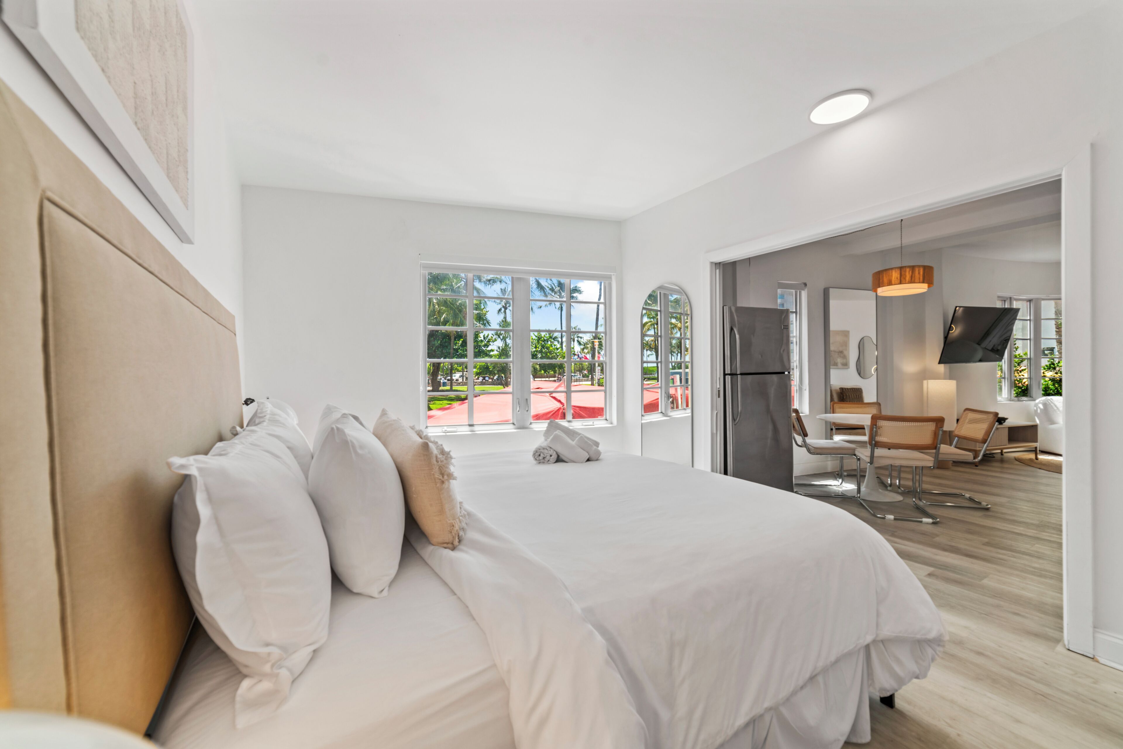 A modern hotel room with a large bed, a dining area, and a view of the outdoors.