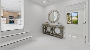 Een modern interieur met een trap, een console tafel met decoratieve objecten, een ronde spiegel en een deur met uitzicht.