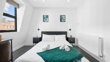 A hotel room with a large bed, two bedside tables, a window with a view, and two wall-mounted artworks.