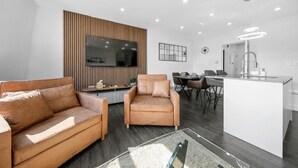 Una sala moderna con sofá, sillón, televisor, comedor y cocina.