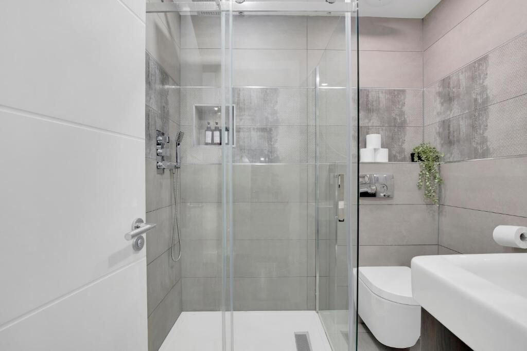 A modern bathroom with a glass-enclosed shower, a toilet, and a sink.