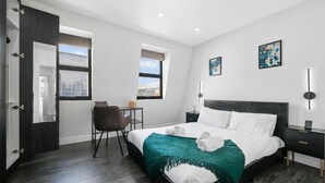 Una habitación de hotel moderna con una cama grande, un escritorio, una silla y dos ventanas.
