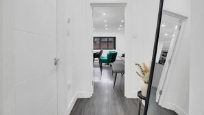 Un pasillo con un comedor al fondo, un espejo a la derecha y una puerta a la izquierda.