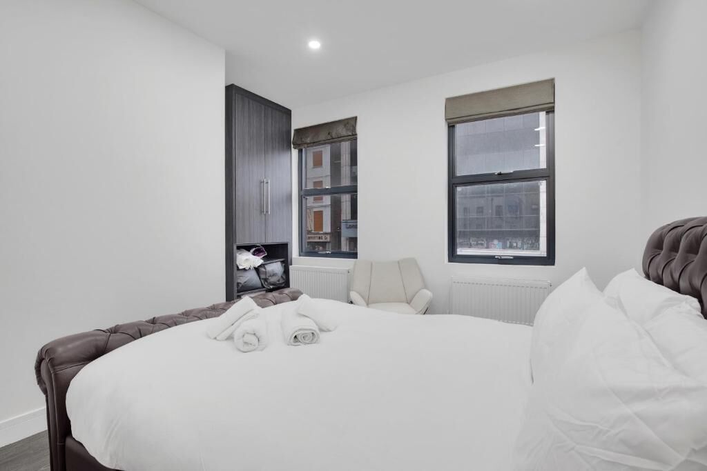 A modern hotel room with a large bed, a seating area with a chair, a television, and a window with a view of buildings.