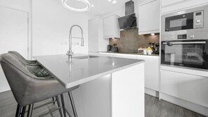Cocina moderna con muebles blancos, una isla central con lavamanos, electrodomésticos de acero inoxidable y una lámpara colgante.