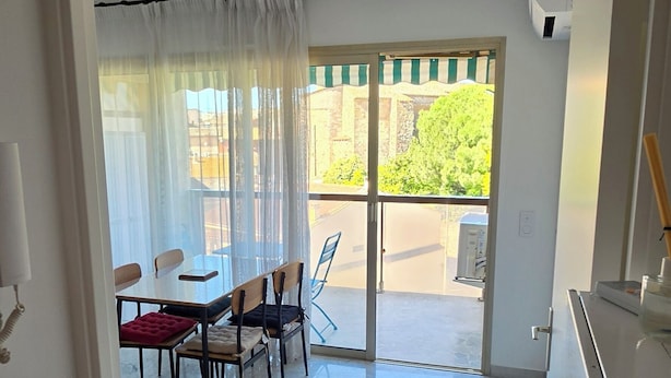 Une pièce dotée d’un sol en marbre, d’un coin repas avec des chaises et une table, d’une porte-fenêtre coulissante donnant sur l’extérieur et d’un climatiseur fixé au mur.
