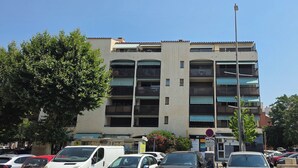 Un immeuble à plusieurs étages doté de balcons, avec des voitures garées et un ciel dégagé.
