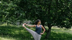 Eine Person führt eine Yoga-Pose im Freien vor Bäumen und Gras aus.