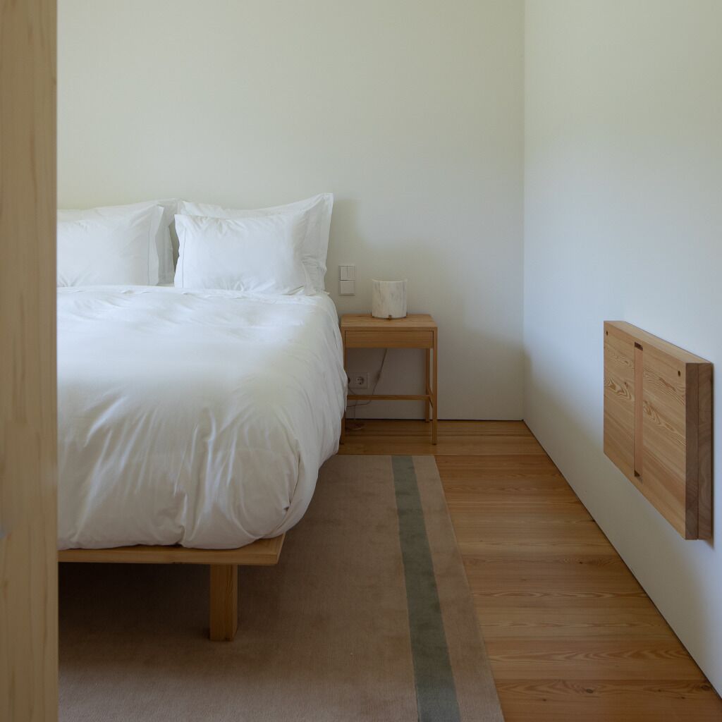 A bedroom with a bed, a nightstand, a lamp, and a bulletin board on the wall.
