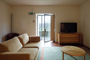 A living room with a sofa, a television on a wooden stand, and a sliding glass door leading to an outdoor area.