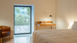 Ein Schlafzimmer mit Bett, Schreibtisch, Stuhl und einem großen Schiebeglasfenster, das auf eine Terrass führt.