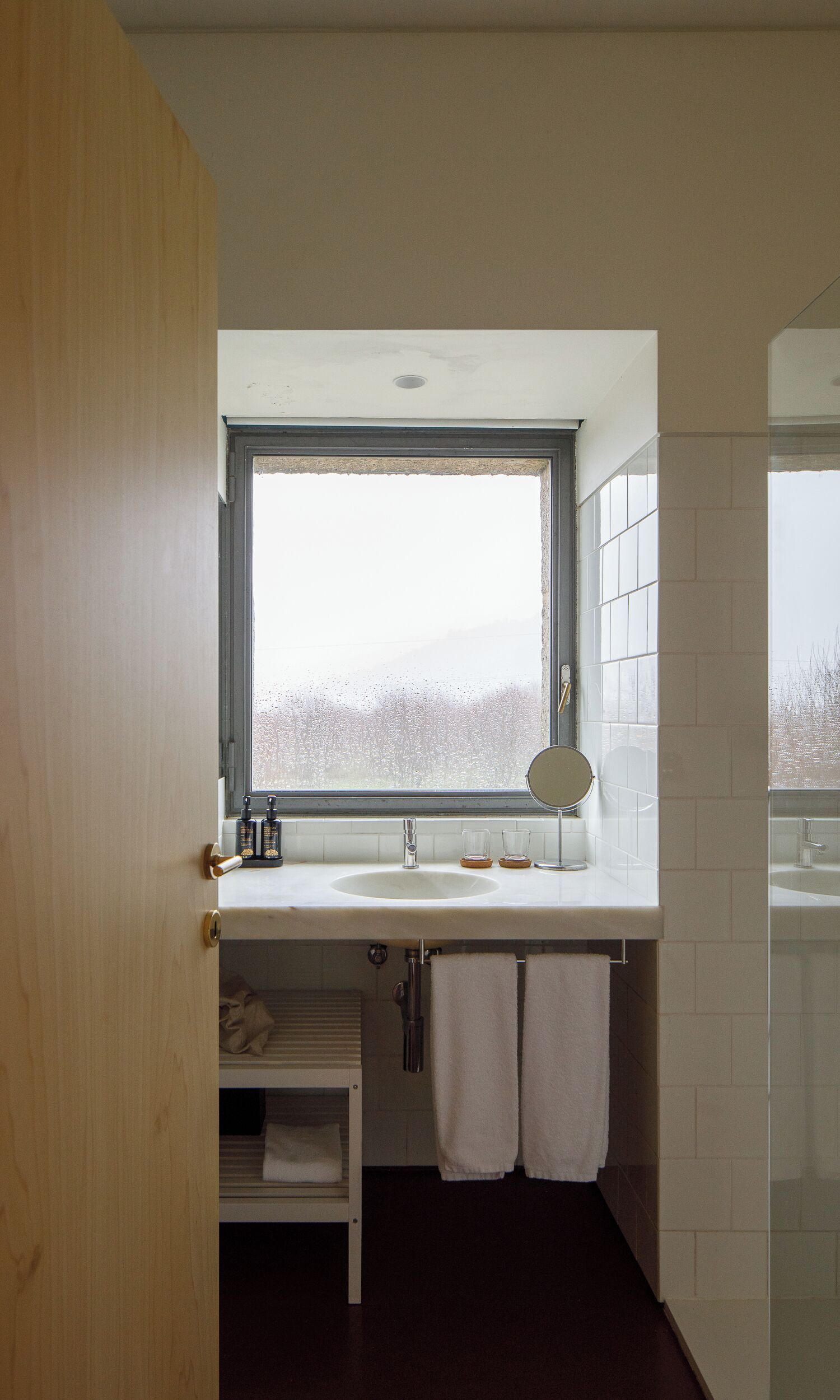 A modern bathroom with a large window, a sink, a mirror, and a towel rack.