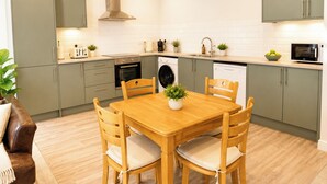 Een moderne keuken met grijze kastjes, een houten eettafel en een inbouwoven.