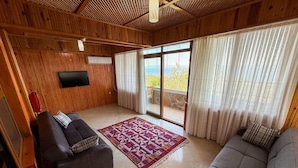 A wooden interior with two sofas, a patterned rug, a flat-screen TV, and a large sliding glass door leading to an outdoor area. - Serinyer Restaurant & Pansiyon (Ayvacik)