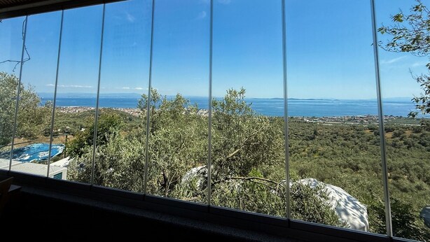 A view through a window with a clear sky, a distant body of water, and a landscape with trees and a building. - Serinyer Restaurant & Pansiyon (Ayvacik)