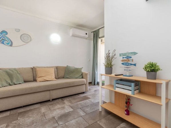 Ein modernes Wohnzimmer mit einem beigefarbenen Sofa, einer Wand-Klimaanlage, einem Wegweiser und einem Holzregal mit einer Topfpflanze.