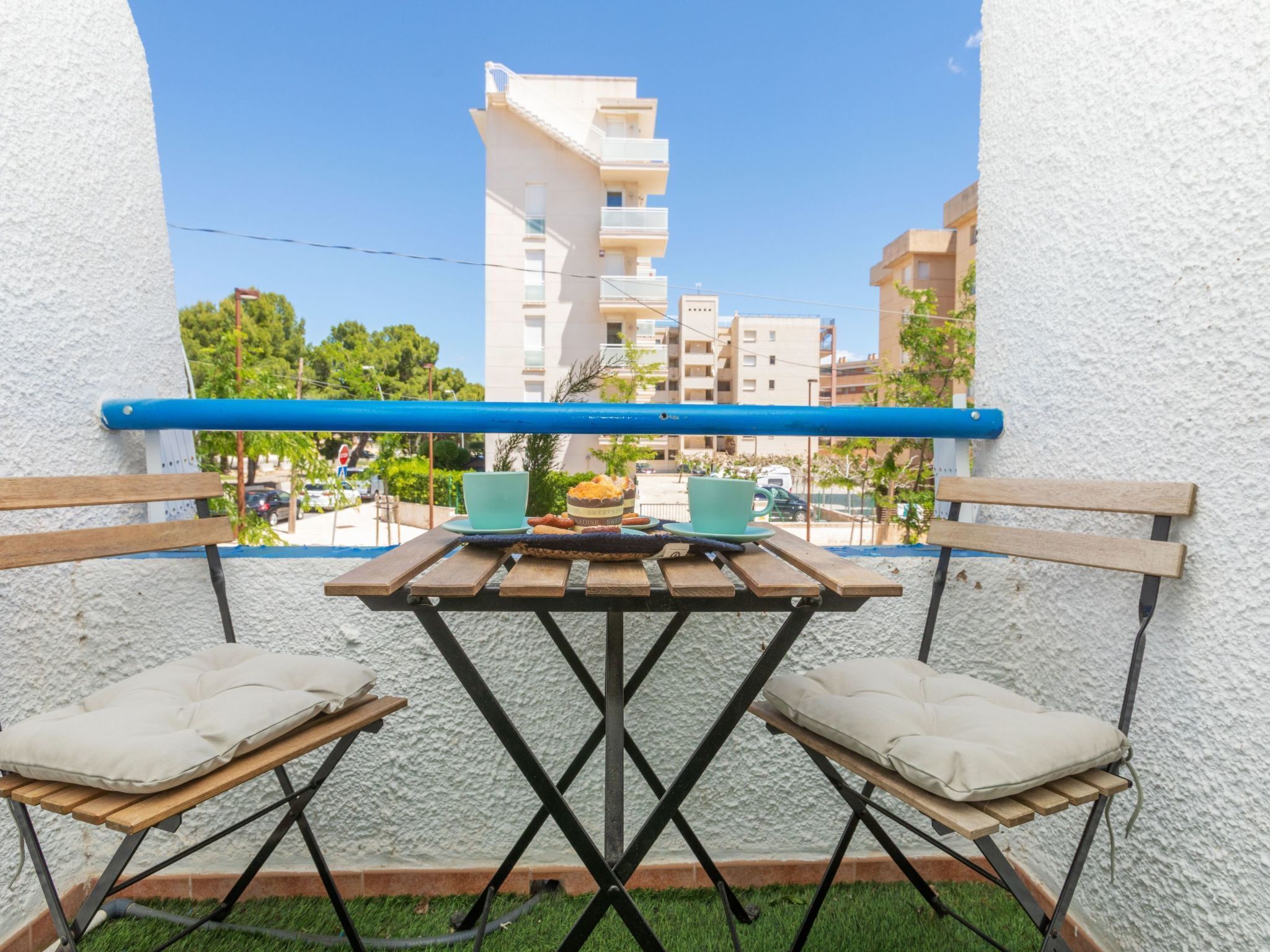 A balcony with a table and two chairs, overlooking a residential area with buildings and trees.