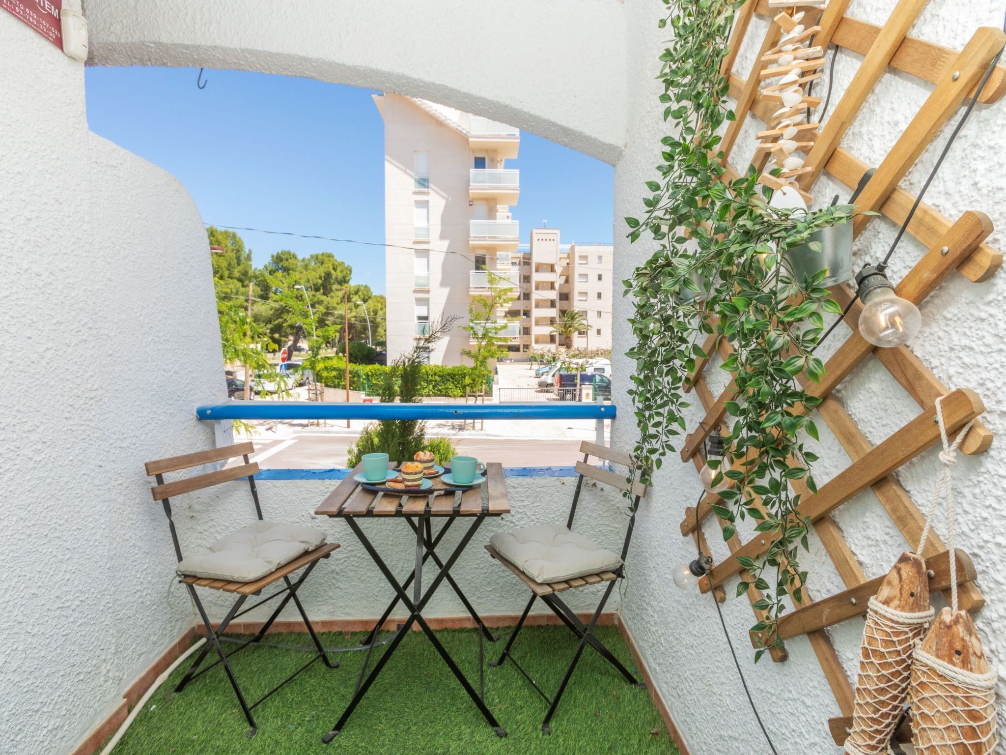 A balcony with a table and chairs, a hanging plant, and a wooden lattice structure.