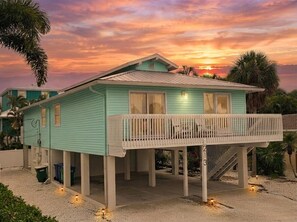 Een gelijkvloers huis met een balkon, een overdekte veranda en een trap naar de bovenverdieping.