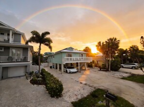 A residential area with a house featuring a balcony, a white car parked in front, and a visible driveway. - Make Beach Memories Luxury AMI House Steps to Sand (Holmes Beach)