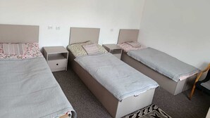 Une chambre avec trois lits simples, chacun étant équipé d’une table de chevet et d’un tiroir.