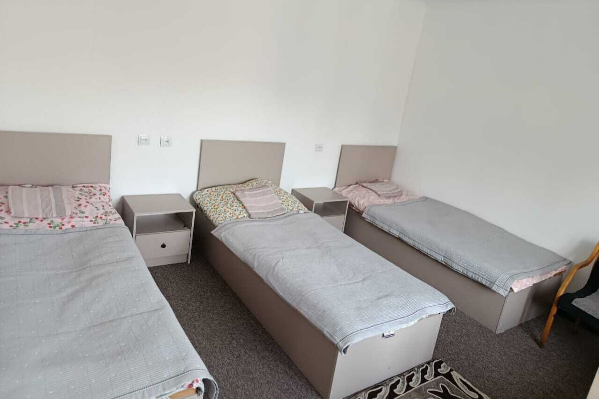 A room with three single beds, each with a nightstand and a drawer.