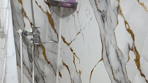 Une salle de bain avec une douche, des murs en marbre et un lavabo blanc.