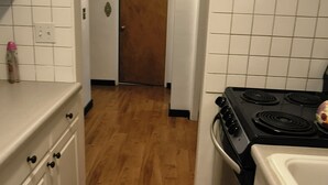 Een keuken met houten vloer, witte kastjes, een fornuis en een deur op de achtergrond.