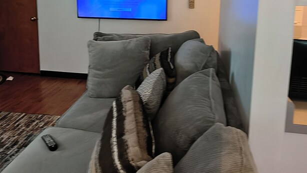 Een woonkamer met een grijze bank, een flatscreen televisie aan de muur en een houten deur.
