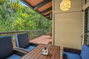 Eine Holzterrasse mit Korbmöbeln und einem Tisch, mit Blick auf einen üppigen Garten.