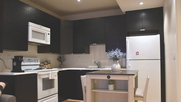 A modern kitchen with dark cabinetry, a white refrigerator, a microwave, and a stove. - Private 2BR Suite | Kitchen & Laundry (Saskatoon)