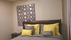 A neatly made bed with a wooden headboard, a decorative wall piece, and a bedside table with a small item on it. - Private 2BR Suite | Kitchen & Laundry (Saskatoon)