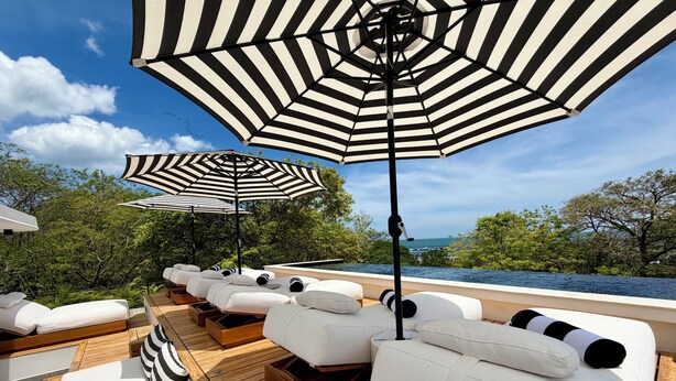 A deck with white lounge chairs and striped umbrellas, overlooking a body of water. - NOAM by the sea Ocean View Suite #2 Adults Only (Tamarindo)