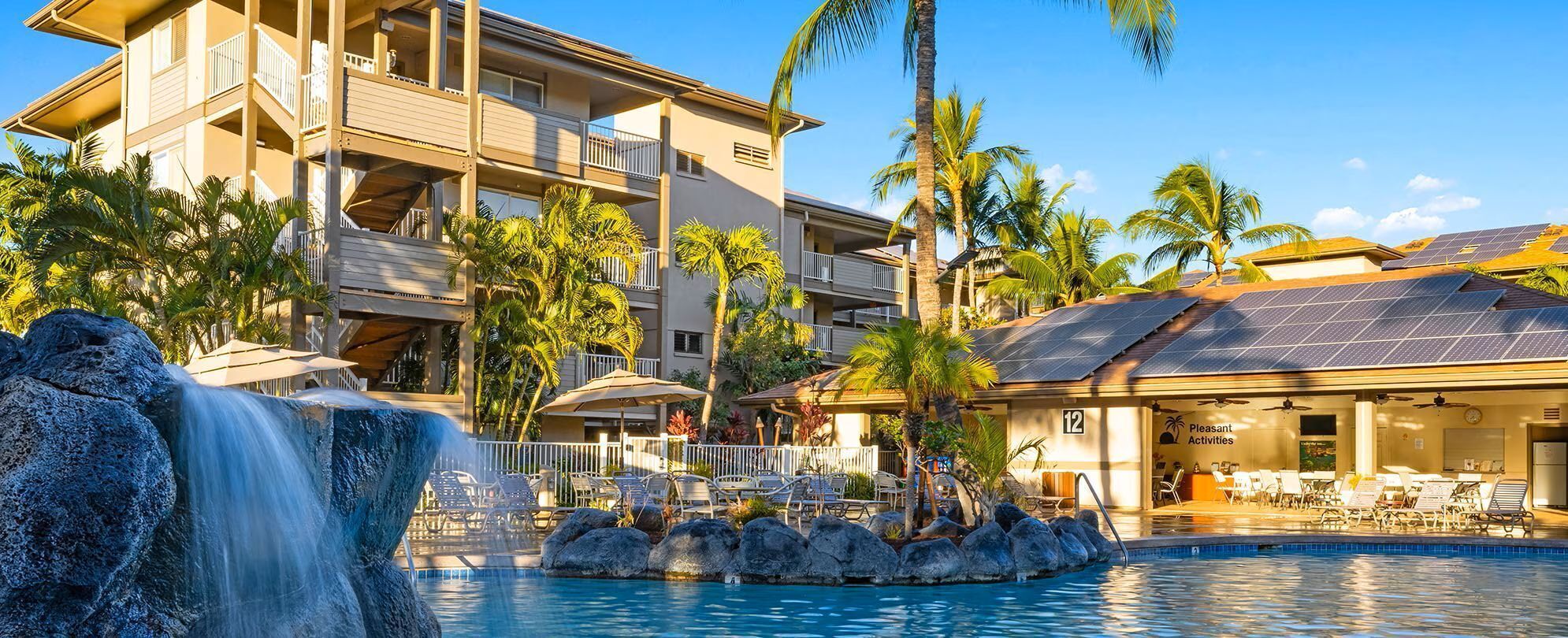 Un hotel con piscina, palmeras, una cascada y paneles solares.
