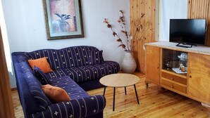 A living room with a sofa, a small round table, a cabinet with a television, and a vase with branches. - Gorgeous 2-bedroom cottage with AC in charming Glossa (Glossa)