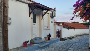 A building with a white facade, a brown door, and a small porch with steps. - Gorgeous 2-bedroom cottage with AC in charming Glossa (Glossa)