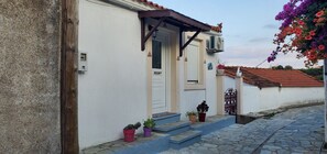 Ein Gebäude mit heller Fassade, einer braunen Tür und einer kleinen Veranda mit Stufen.