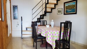 A dining area with a table set for four, a staircase, and a painting on the wall. - Gorgeous 2-bedroom cottage with AC in charming Glossa (Glossa)