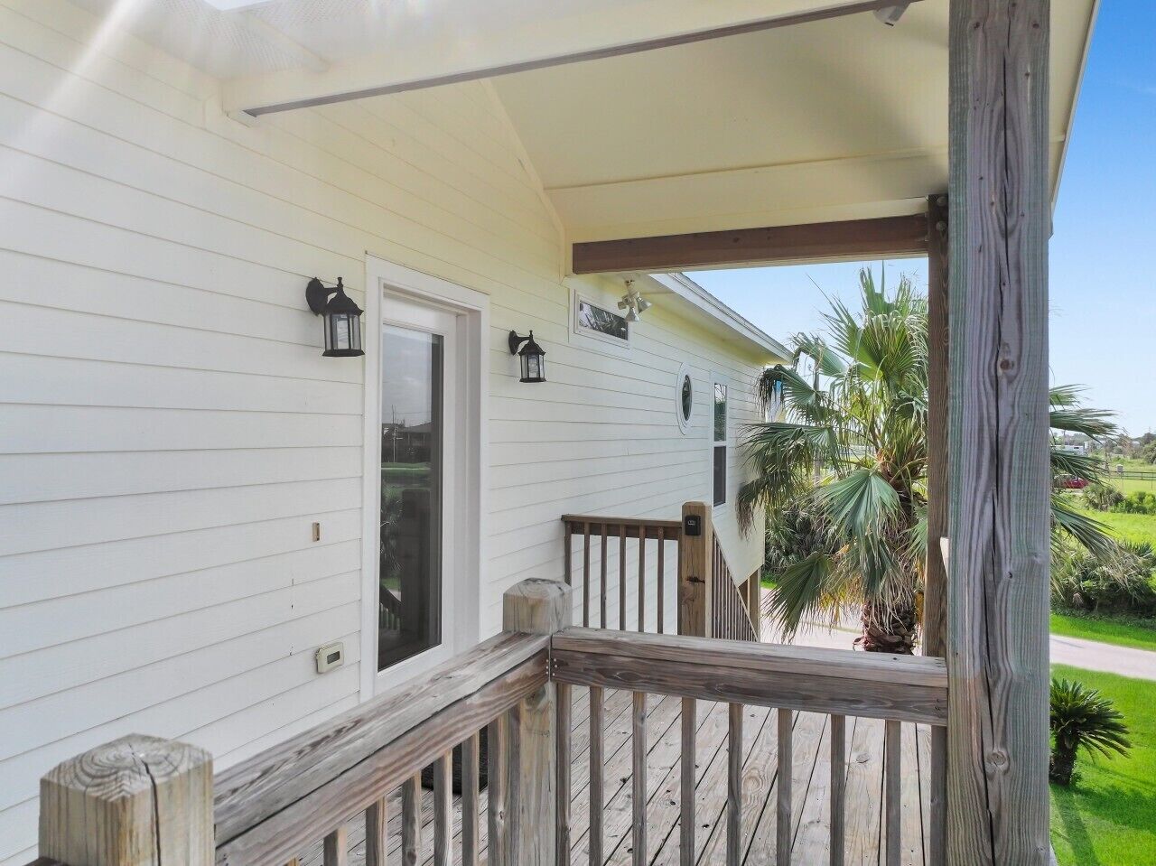 A wooden deck with railings, a door, and two wall-mounted lanterns.