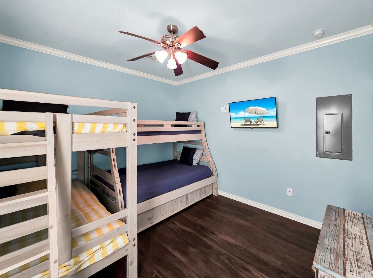 Une pièce avec des lits superposés, un ventilateur de plafond, un tableau et un interrupteur sur le mur.