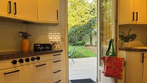 Eine Küche mit weißen Schränken, einer Kaffeebar und Blick auf einen Garten durch eine Glastür.