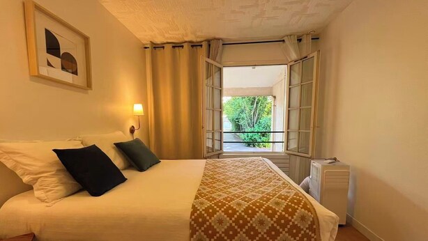 Ein Schlafzimmer mit Bett, Nachttisch, Lampe, einem Fenster mit Vorhängen und einer Heizung.