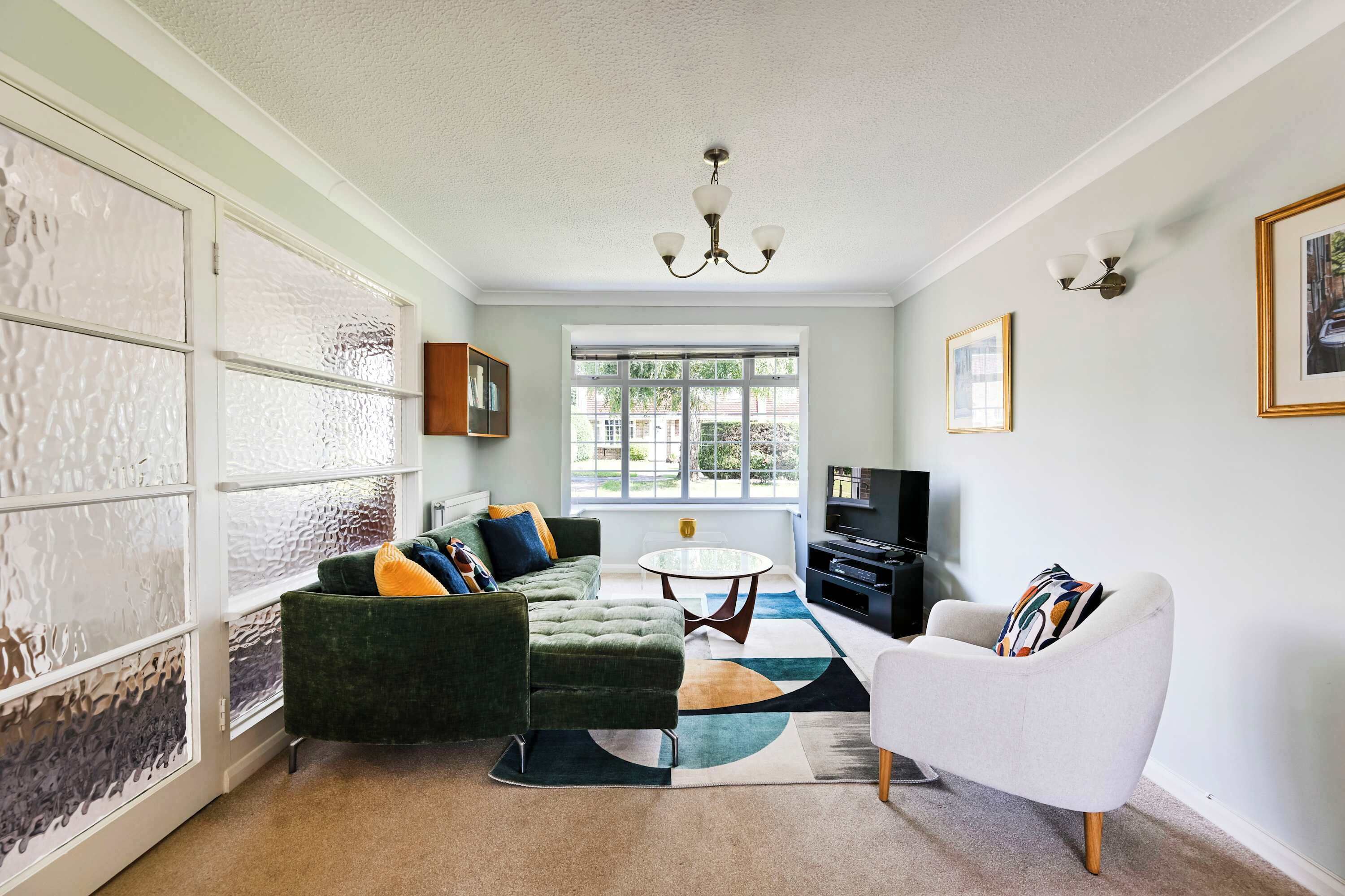 A living room with a green sofa, a white armchair, a round coffee table, and a TV.