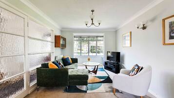 A living room with a green sofa, a white armchair, a round coffee table, and a TV.