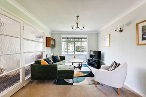A living room with a green sofa, a white armchair, a round coffee table, and a TV. - Spacious 3Bed Home in Maidenhead  Sleeps 6 (Maidenhead)